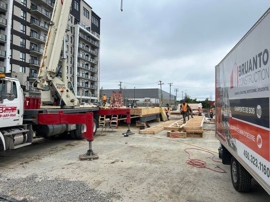 Chantier de construction avec un camion-pompe à béton, une équipe de travailleurs et des palettes de bois.