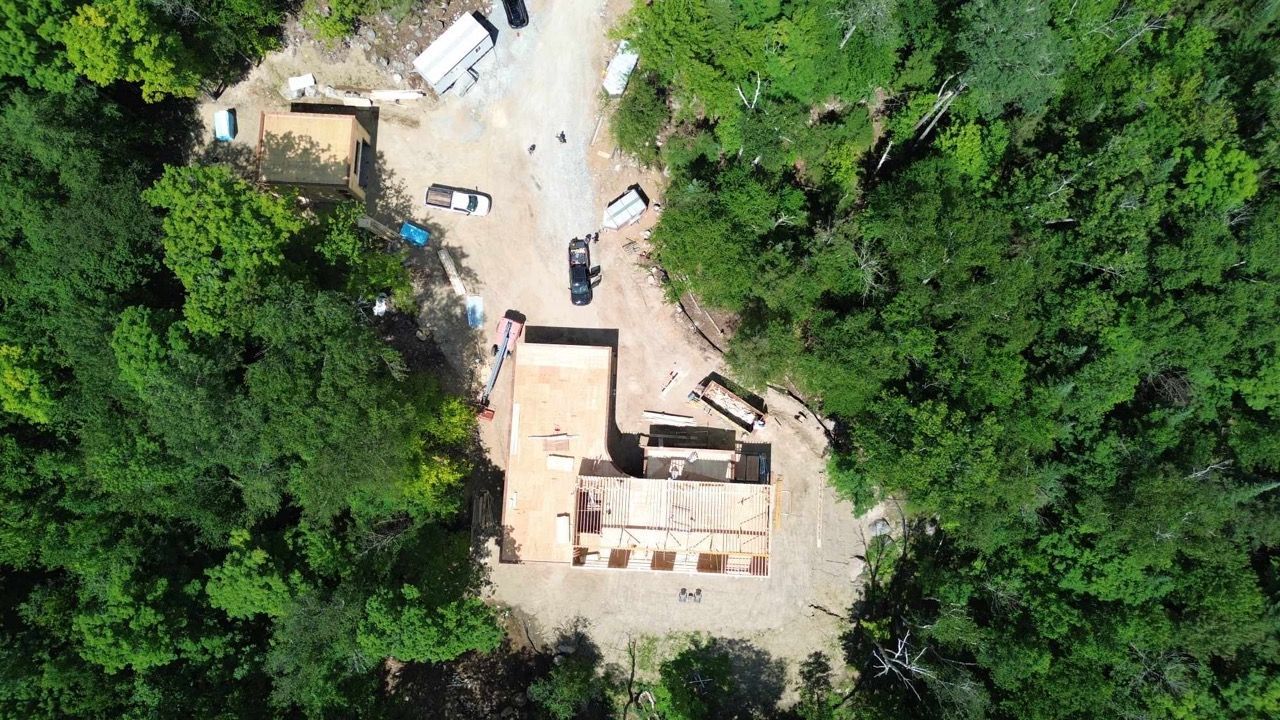 Vue aérienne d'un bâtiment en construction, entouré d'arbres et d'un chemin de terre.