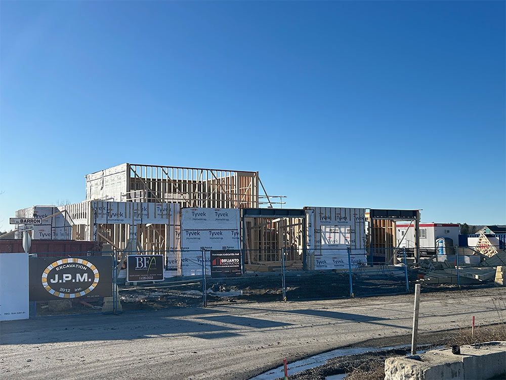 Chantier : bâtiment à ossature bois en construction, ciel bleu et panneau JPM au premier plan.