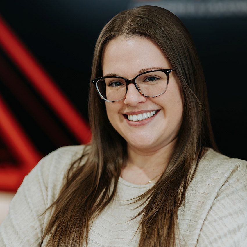 Une femme portant des lunettes sourit à l'objectif devant un fond rouge et noir.