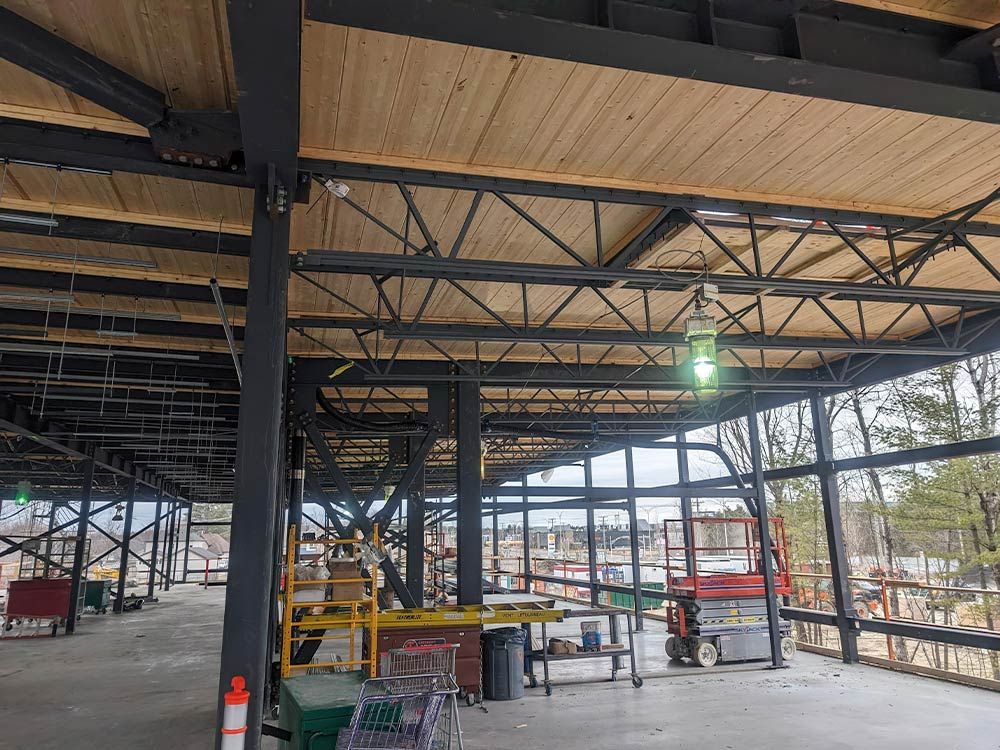 Chantier de construction à ossature métallique, plafond en bois apparent et éclairage vert, en extérieur.