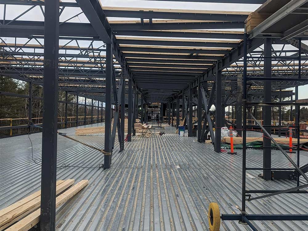 Charpente métallique d'un bâtiment en construction, plancher en tôle ondulée, poutres en bois, ciel couvert.