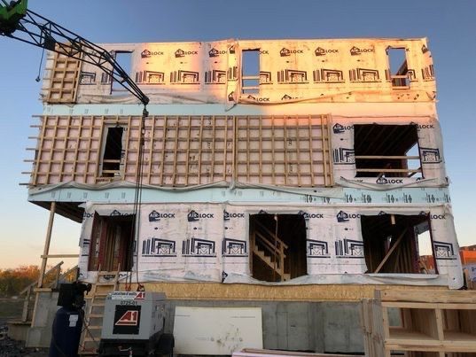 Immeuble de plusieurs étages en construction avec une grue au coucher du soleil. Charpente en bois, fenêtres et isolation visibles.