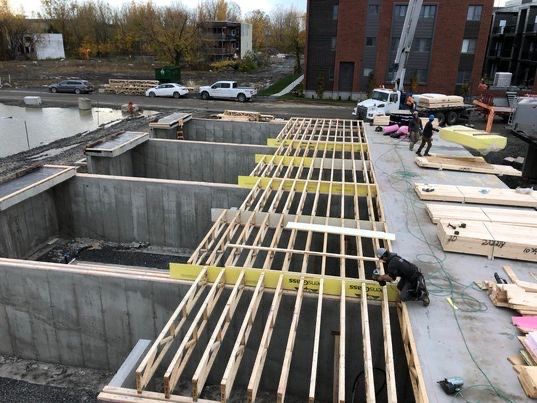 Chantier de construction : Ouvriers construisant une charpente en bois au-dessus de structures en béton.