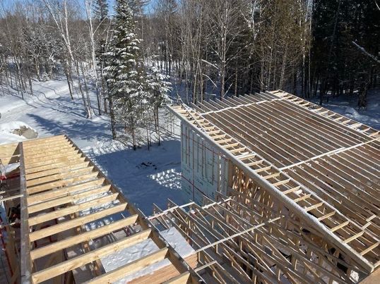 Chantier de construction avec charpente de toit en bois apparente dans une forêt enneigée.