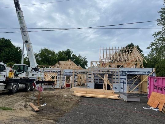 Chantier de construction avec une grue soulevant des matériaux ; charpente en bois d'une maison en construction.