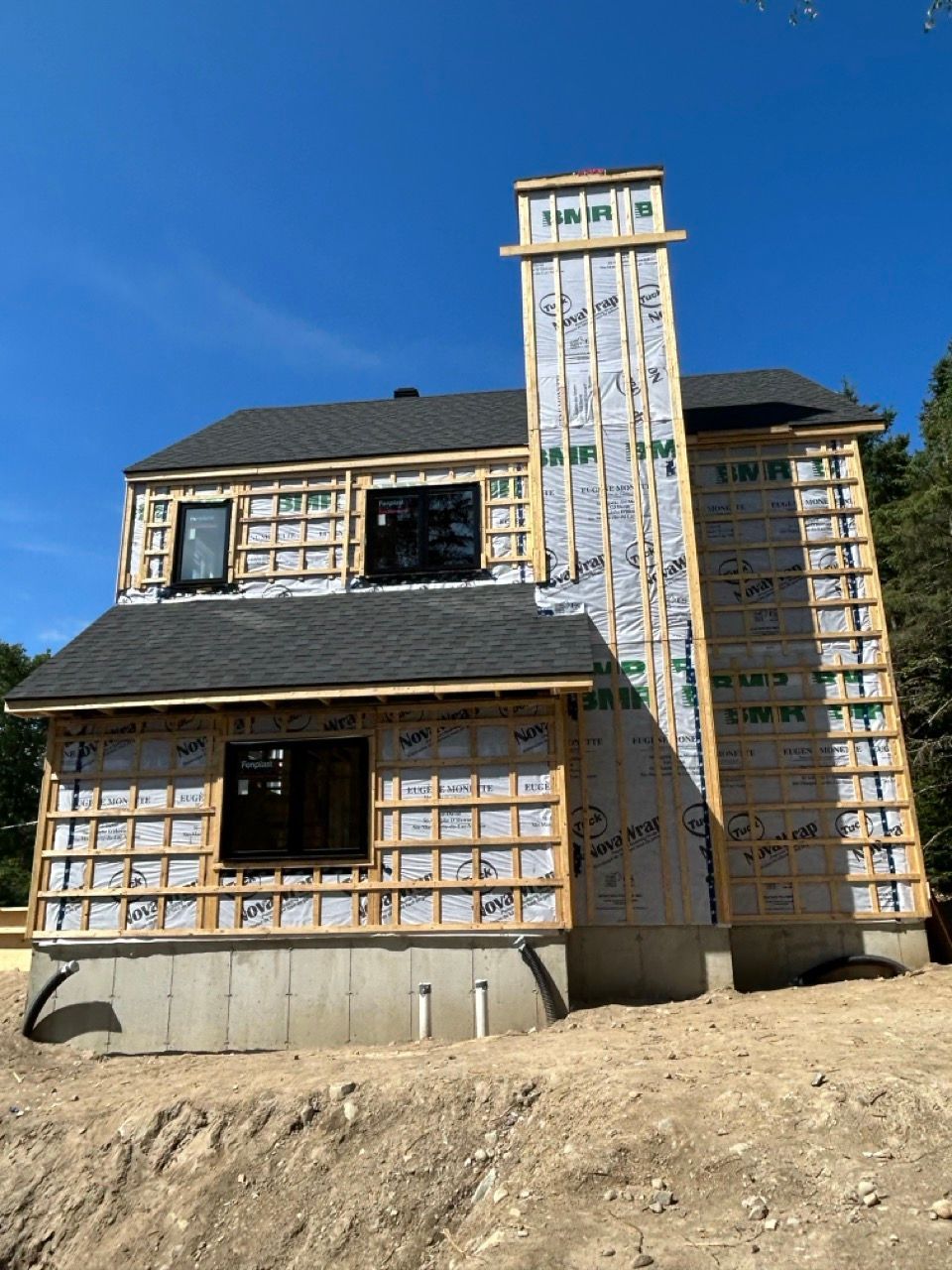 Maison à deux étages en construction avec cheminée. Toiture, bardage et fondations noirs. Ciel dégagé et ensoleillé.