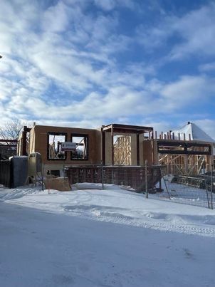 Construction d'une ossature de maison en hiver. Neige au sol, ciel bleu, structure en bois avec ouvertures pour fenêtres.