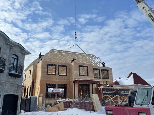 Chantier de construction. Une maison en bois de deux étages en construction, une grue soulevant la charpente du toit par une journée enneigée.