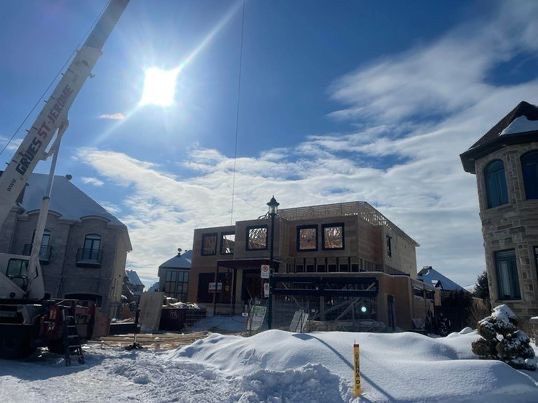 Construction d'une maison à deux étages, grue présente, sous un ciel bleu ensoleillé avec de la neige au sol.