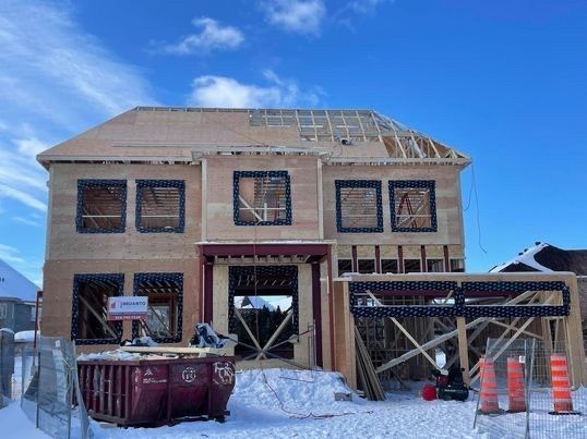 Maison en construction par une journée enneigée, avec une structure en bois et des fenêtres vides.