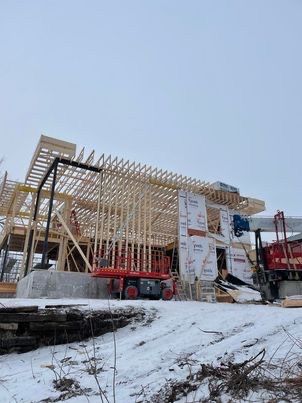 Bâtiment en construction dans un décor enneigé, avec une nacelle élévatrice et une structure partiellement charpentée.