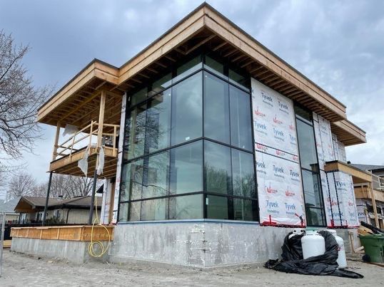 Maison moderne en construction avec de grandes baies vitrées et des éléments en bois, par temps nuageux.