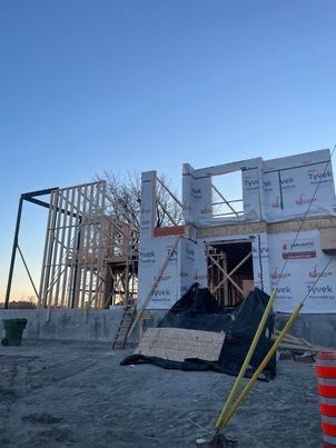 Chantier de construction : bâtiment à ossature bois recouvert d’un film Tyvek et charpente apparente sur fond de ciel bleu.