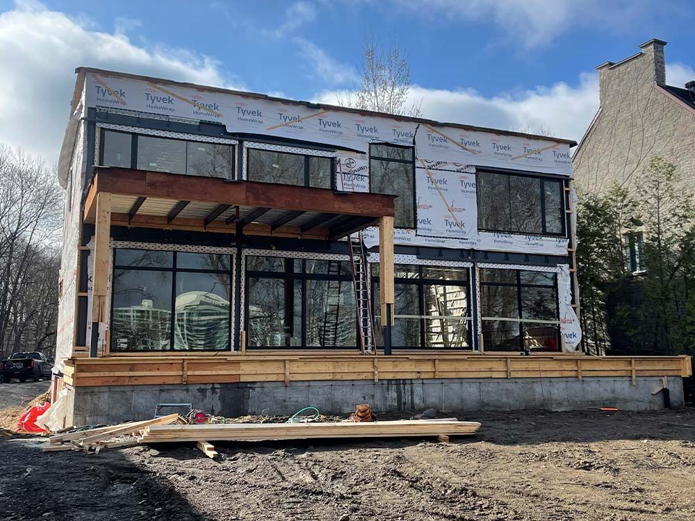 Maison à deux étages en construction, avec de grandes fenêtres, une terrasse et un porche en bois.