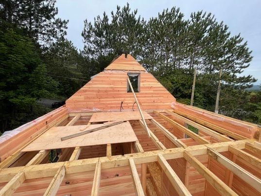Construction d'une toiture de maison, utilisant des poutres et un platelage en bois. Une partie de la toiture en A est construite dans un environnement boisé.