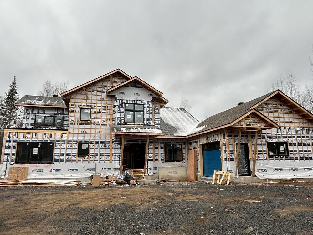 Maison en construction, ossature bois, revêtement bleu, fenêtres sombres, ciel nuageux.