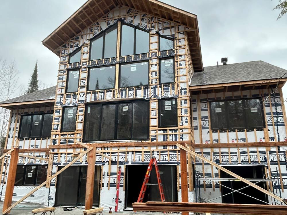 Maison en construction, avec de grandes fenêtres, recouverte d'un matériau d'étanchéité et d'échafaudages.