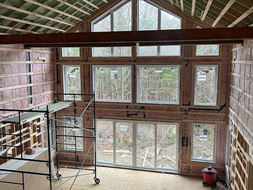 Intérieur d'un bâtiment en construction, avec de grandes fenêtres et des échafaudages ; l'isolation est visible.