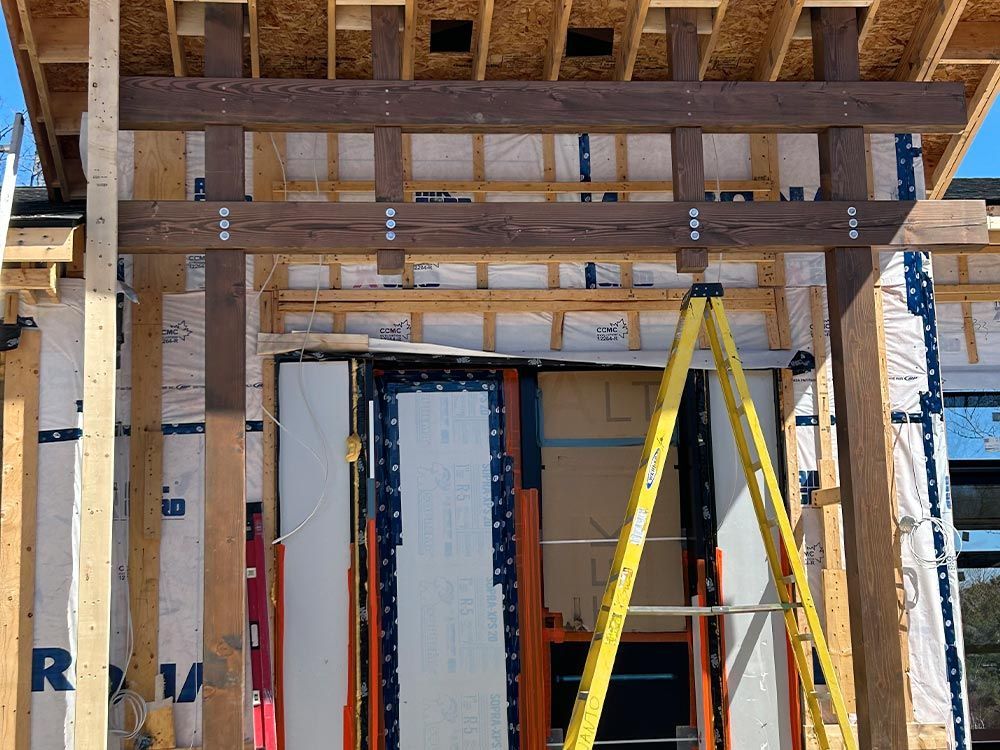 Chantier : des poutres en bois soutiennent une porte, une échelle est visible au premier plan.