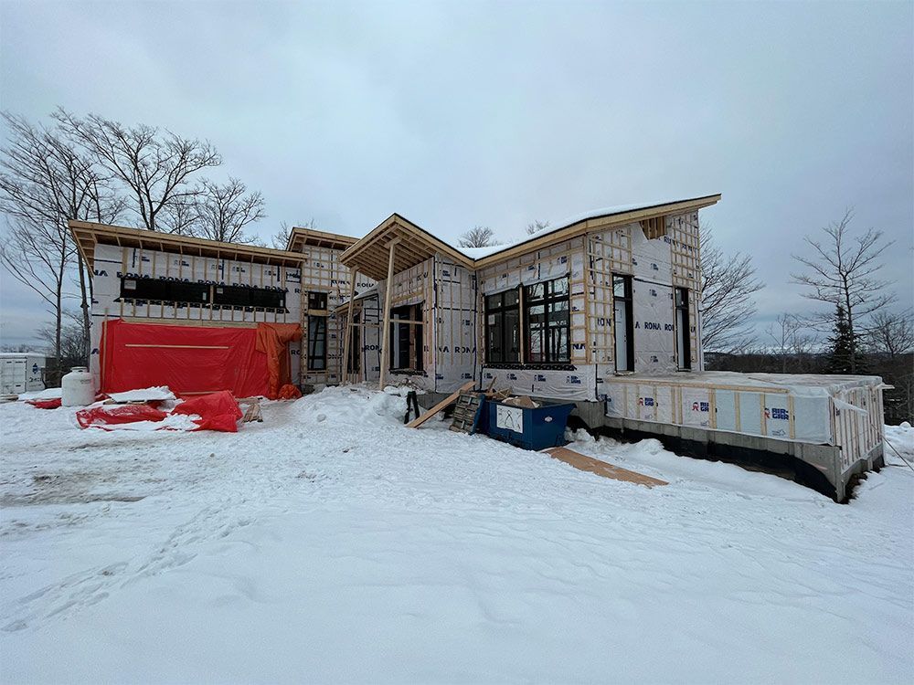 Maison en construction dans un décor enneigé ; on aperçoit la charpente en bois et les fenêtres noires.