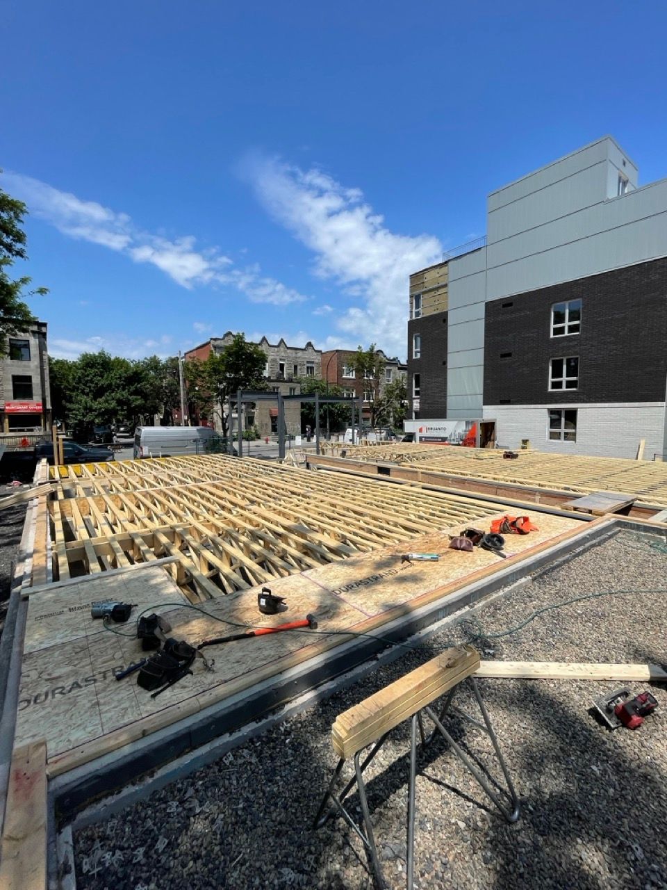 Chantier de construction avec charpente en bois, bâtiments en arrière-plan, ciel bleu.