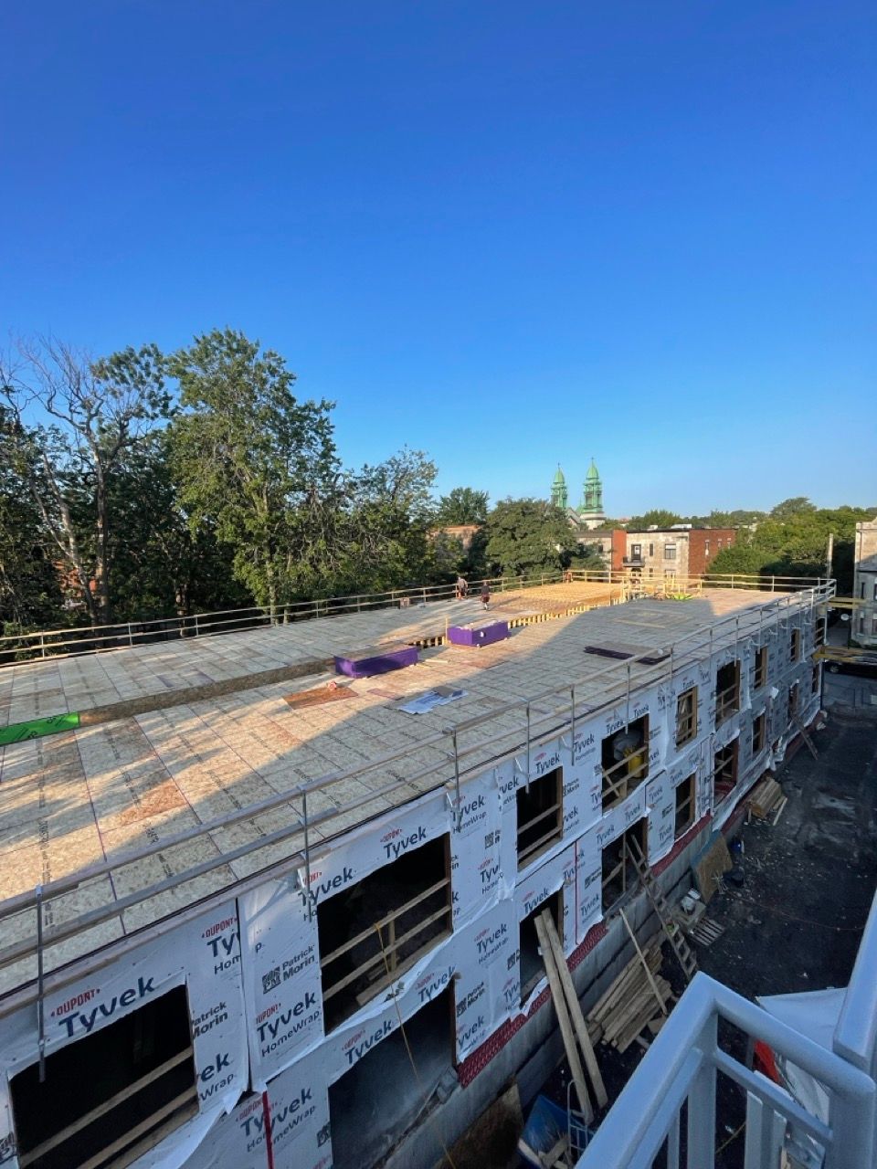 Chantier de construction avec un bâtiment de deux étages partiellement construit ; ciel bleu et arbres en arrière-plan.