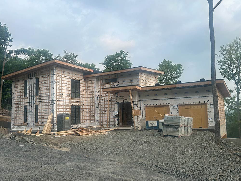 Maison en construction avec charpente apparente, garage et allée de gravier.