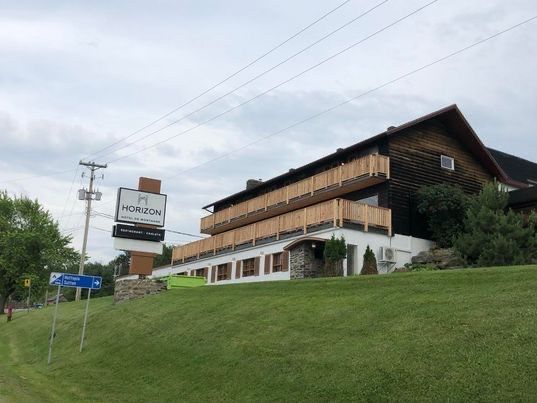 Bâtiment d'hôtel avec balcons en bois et enseigne, situé sur une colline herbeuse sous un ciel couvert.