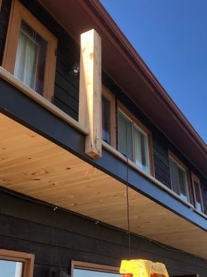 Poutre en bois soutenant le toit d'un bâtiment au bardage noir et comportant de nombreuses fenêtres.