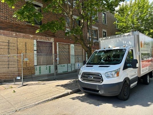 Camion de livraison blanc stationné dans une rue près d'un bâtiment aux fenêtres et portes condamnées.