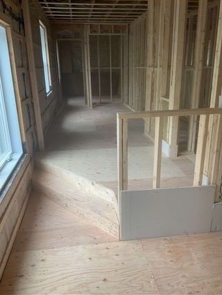 Vue intérieure d'un bâtiment en construction, montrant la charpente en bois, les sols non finis et les portes.