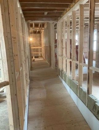 Ossature intérieure d'un couloir en construction ; montants en bois, isolation et planchers non finis visibles.
