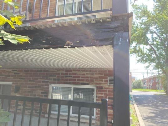 Vue extérieure d'un bâtiment avec un auvent délabré, une façade en briques et une balustrade noire.