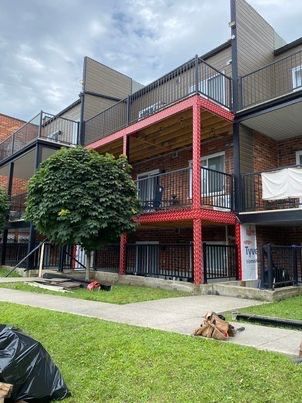 Immeuble d'appartements avec balcons à encadrement rouge, balustrades noires et pelouse verte sous un ciel nuageux.