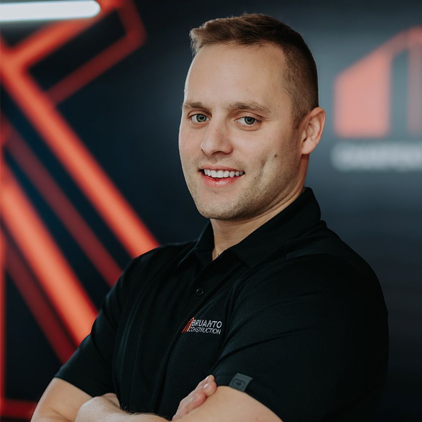 Homme souriant portant un polo noir. Logo de l'entreprise sur le polo ; fond géométrique orange et noir.