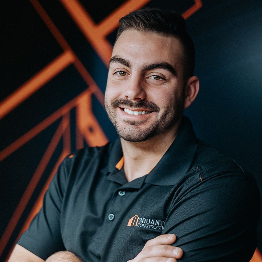 Homme souriant portant un polo noir. Logo de l'entreprise sur le polo ; fond géométrique orange et noir.