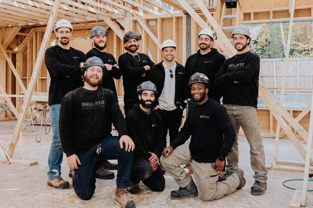 Des ouvriers du bâtiment, casqués, posent devant une structure à ossature bois, certains souriants, vêtus de chemises noires.