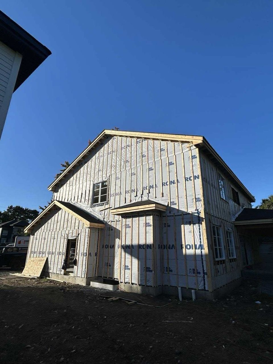 Maison à deux étages en construction, revêtement et cadres de fenêtres visibles, sur fond de ciel bleu clair.