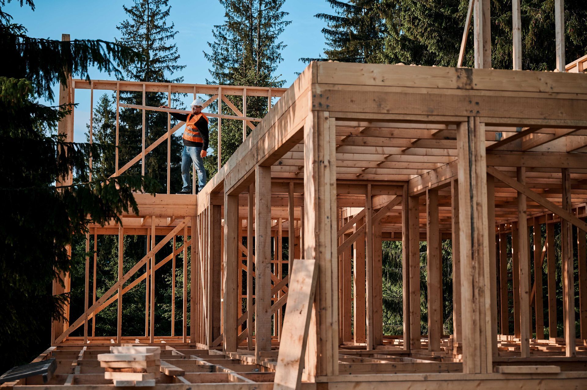 La structure en bois d'une maison est en construction ; un ouvrier se trouve à l'étage supérieur.