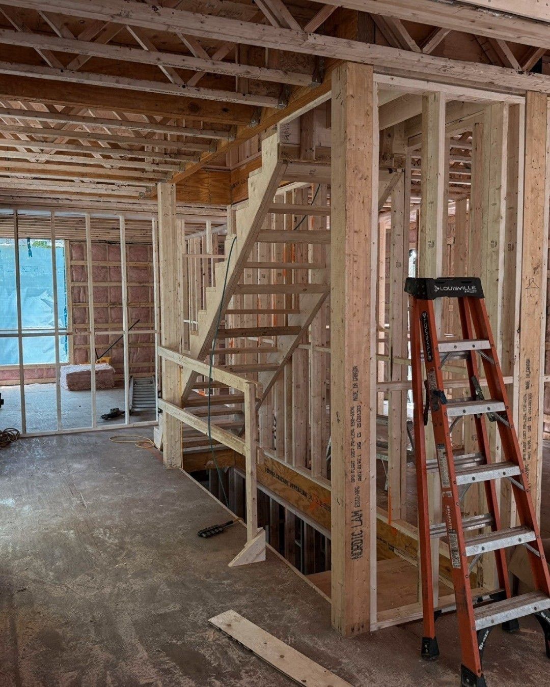 Escalier en bois en construction à l'intérieur d'une structure de bâtiment ; une échelle orange est appuyée contre le mur.