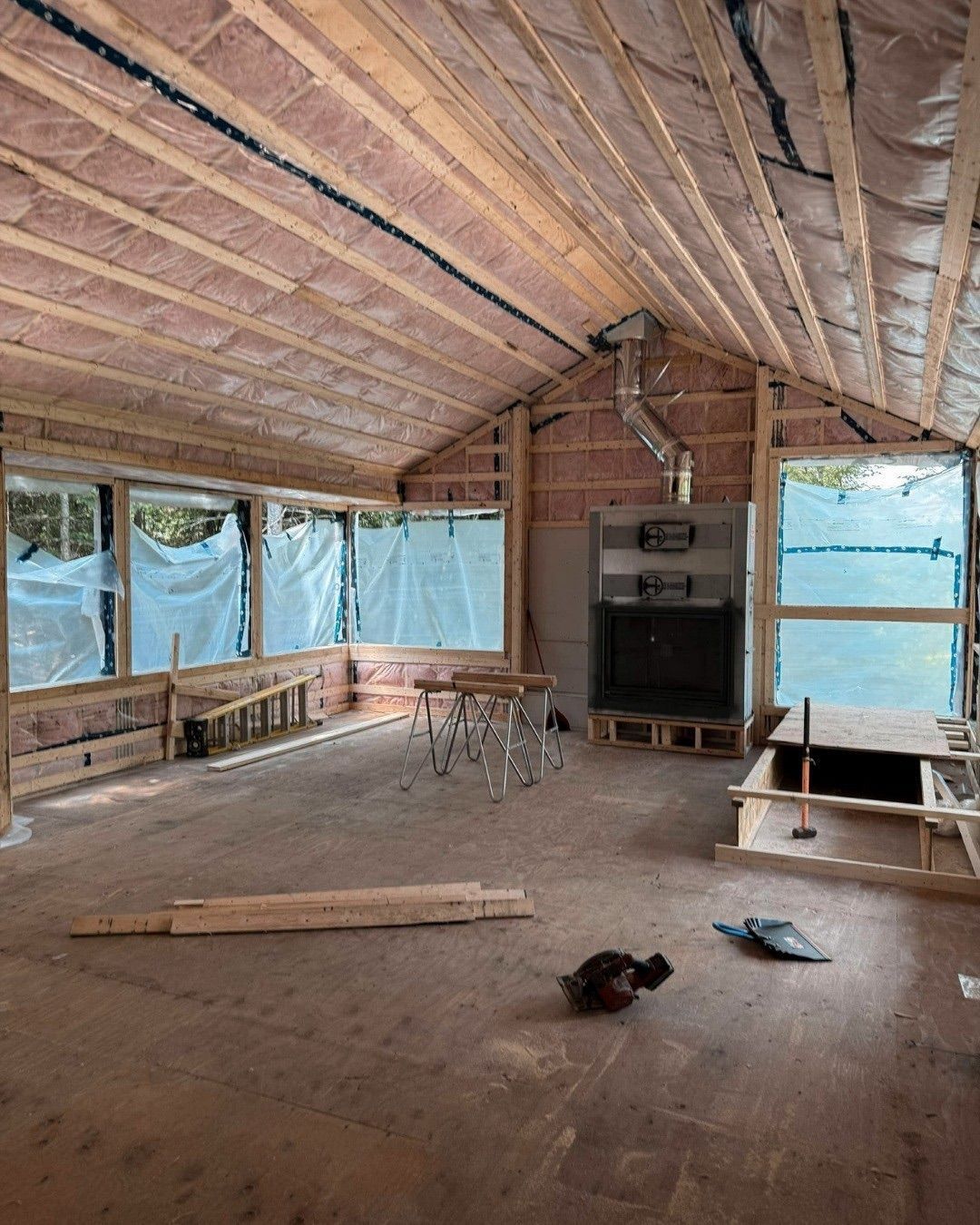 Intérieur d'une pièce en construction, avec charpente en bois apparente, isolation et fenêtres.