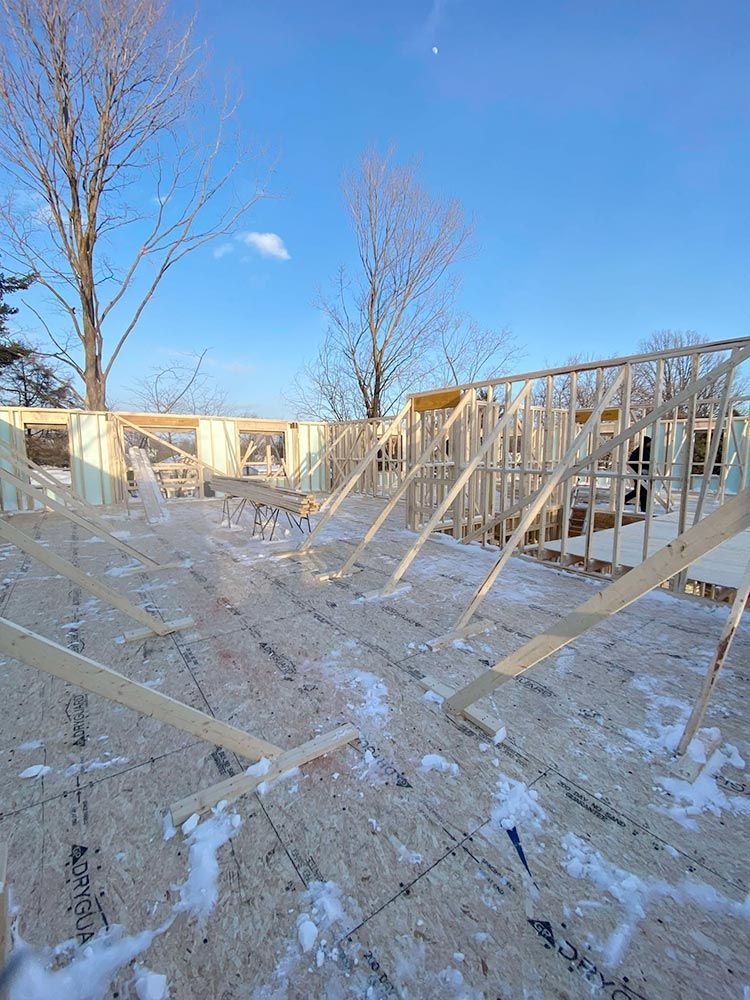 Charpente en bois d'un bâtiment en construction sur une surface enneigée sous un ciel bleu.