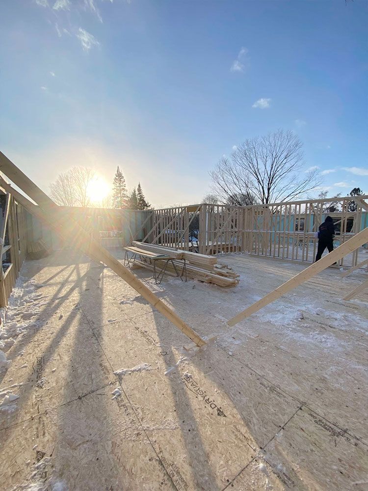 Chantier de construction avec charpente en bois et une personne travaillant par une journée ensoleillée et enneigée.