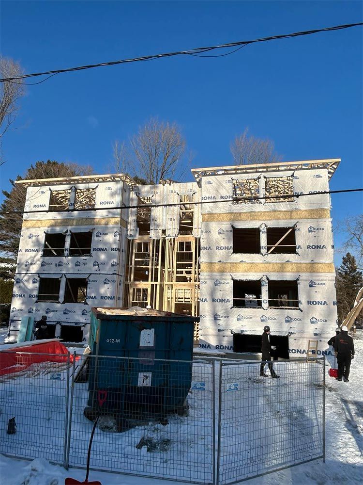 Bâtiment en construction, trois étages, ossature bois, recouvert de bâche blanche. Chantier en activité, neige au sol.