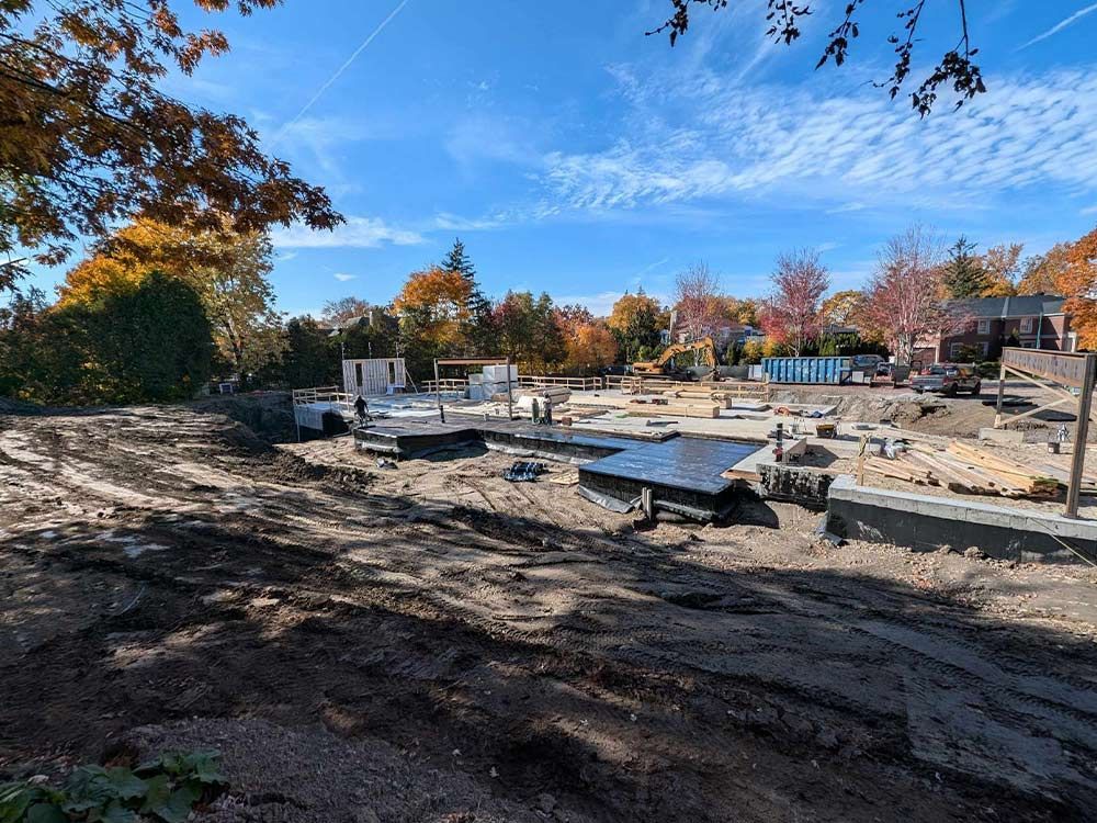 Chantier de construction avec travaux de fondation. Terre brune, blocs de béton et une structure en construction sous un ciel bleu aux couleurs d'automne.