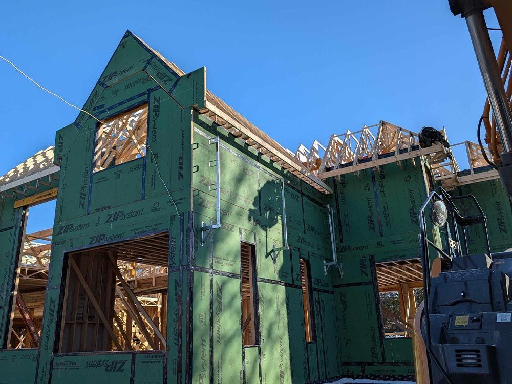 Construction d'une maison avec un revêtement vert et une charpente en bois apparente sur fond de ciel bleu.