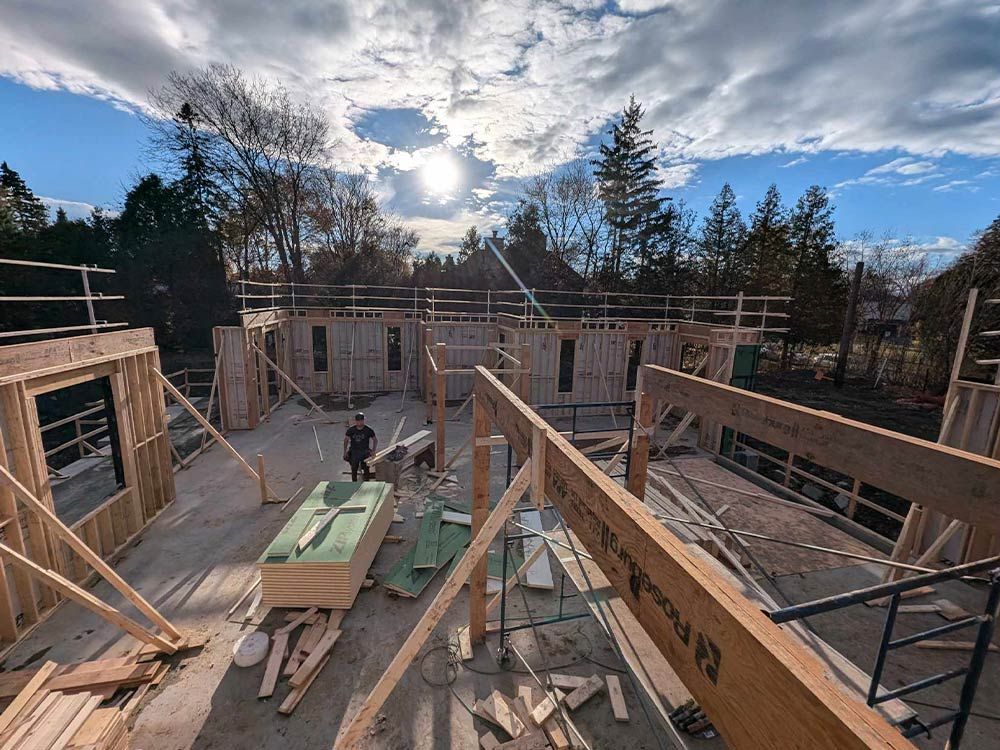 Chantier de construction, charpente en bois d'un bâtiment sous un ciel lumineux. Un ouvrier se tient à proximité.