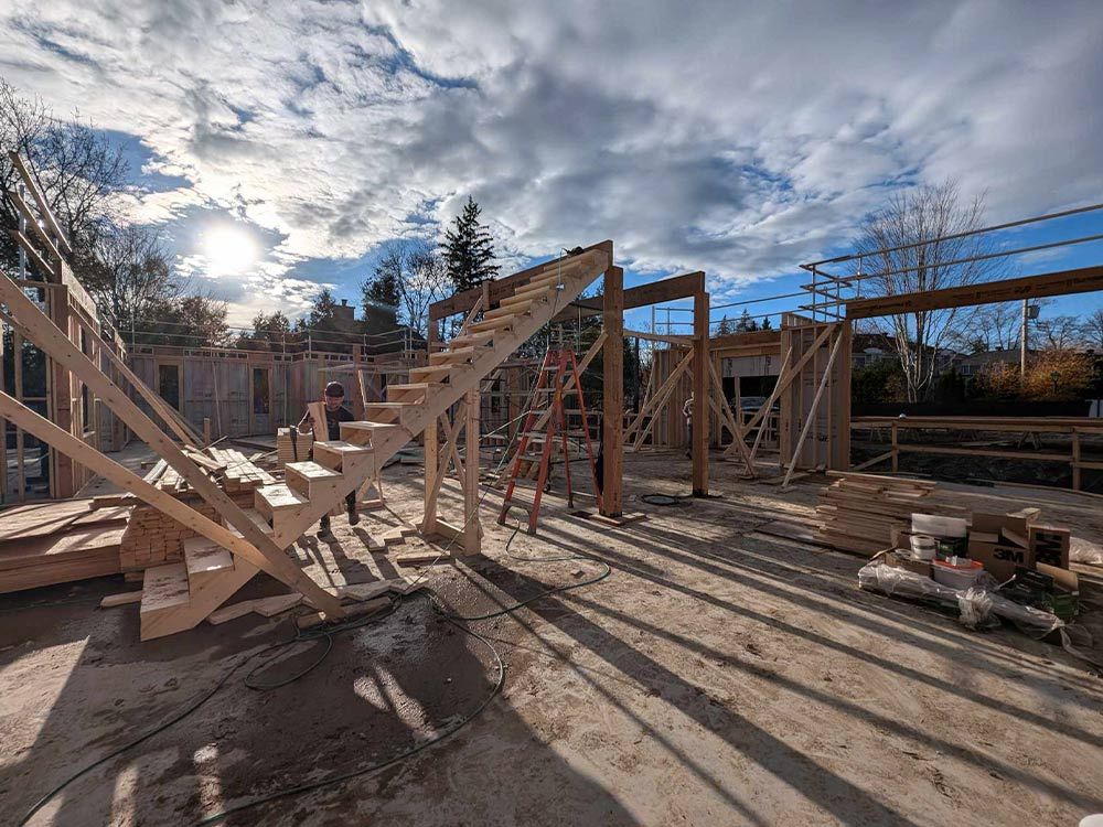 Chantier de construction avec charpente en bois, escalier et ciel nuageux.