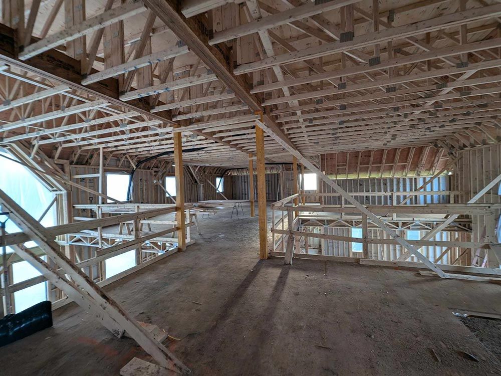 Vue intérieure d'un bâtiment en construction, montrant la charpente en bois apparente des murs, du plafond et de la passerelle.